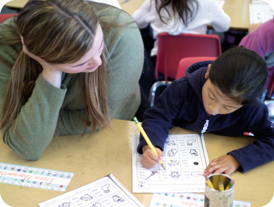Child learning to write with a teacher in a classroom